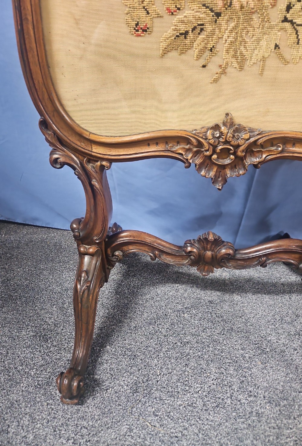 A Victorian carved walnut fire screen featuring an ornate cresting frame supported by cabriole legs, encasing a floral needlepoint textile panel. View X