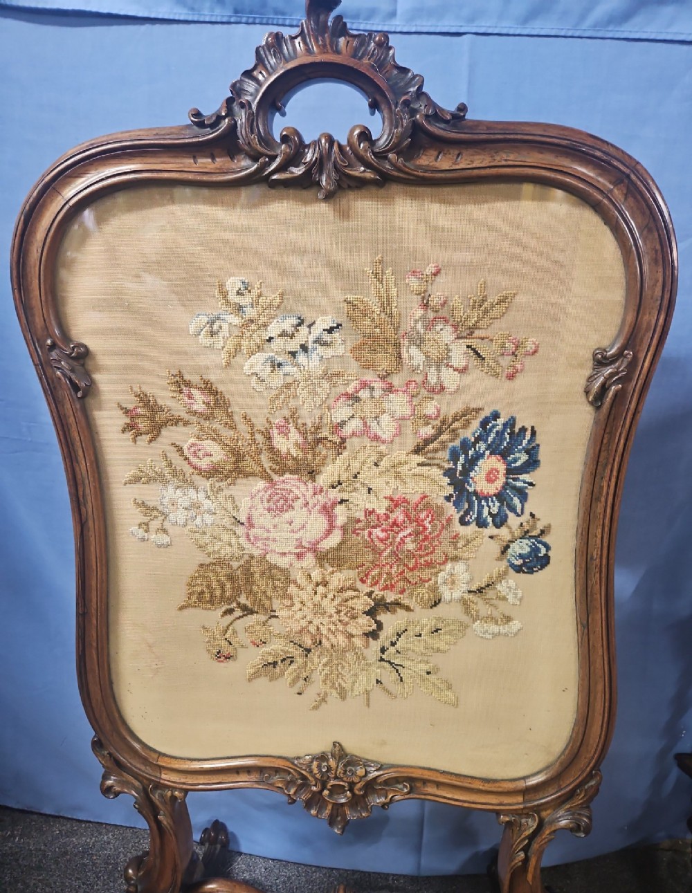 A Victorian carved walnut fire screen featuring an ornate cresting frame supported by cabriole legs, encasing a floral needlepoint textile panel. View XI