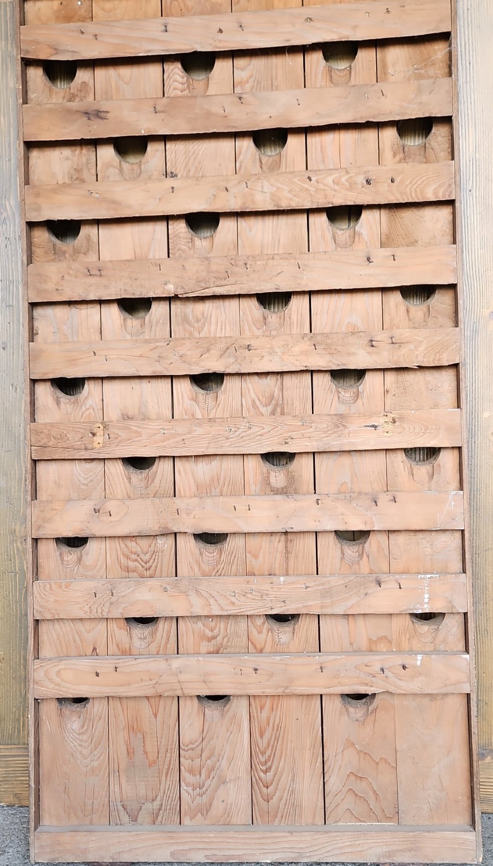 A vertical weathered timber champagne riddling rack featuring multiple angled circular cutouts and stamped with Champagne Mumm Reims France near the base. View III