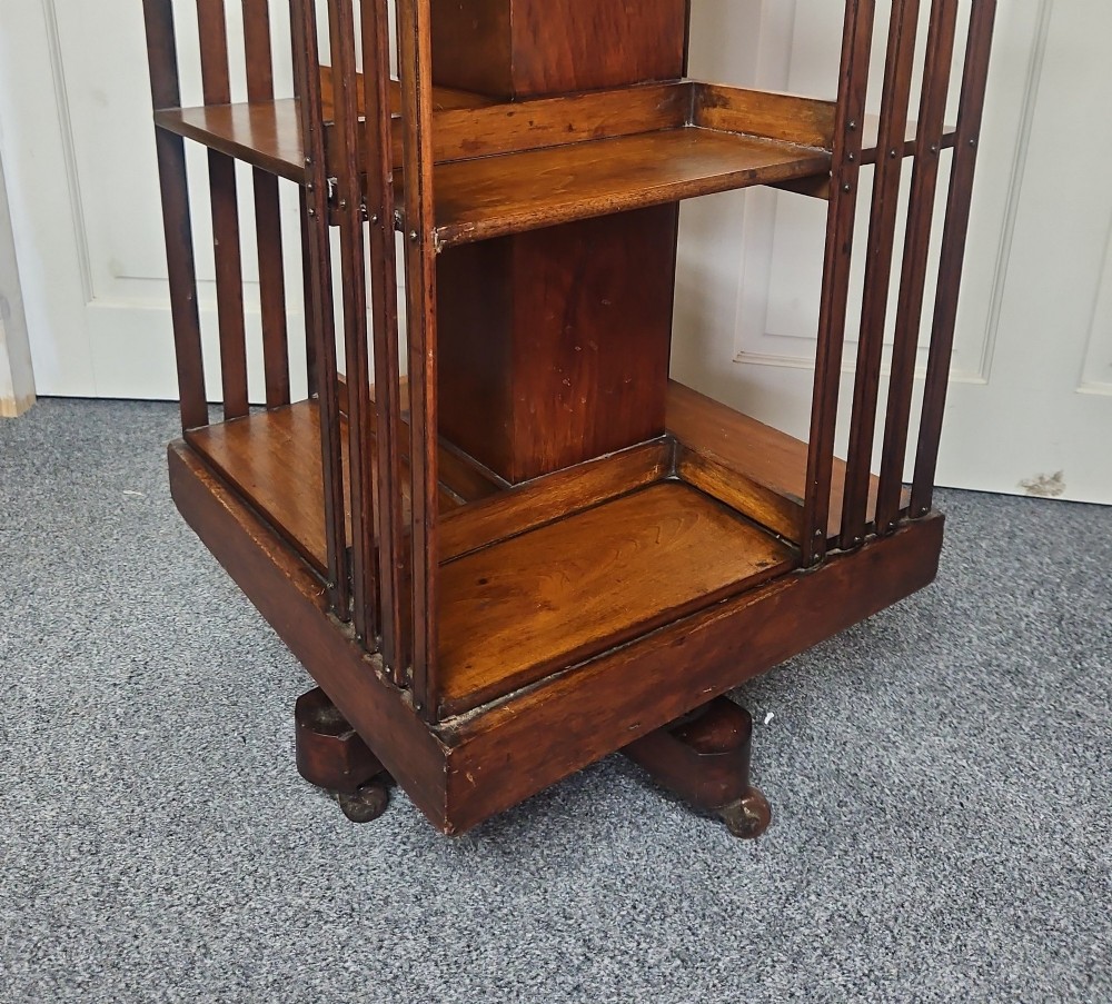 An Edwardian mahogany revolving bookcase featuring vertical slatted sides, two tiers of open shelving, and a square moulded top set on a rotating cross base. View II