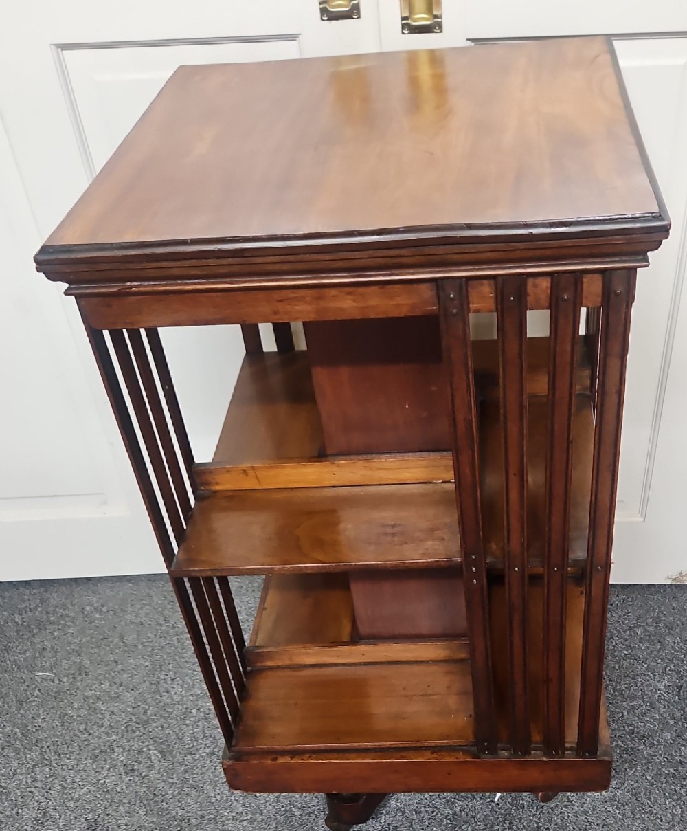 An Edwardian mahogany revolving bookcase featuring vertical slatted sides, two tiers of open shelving, and a square moulded top set on a rotating cross base. View V