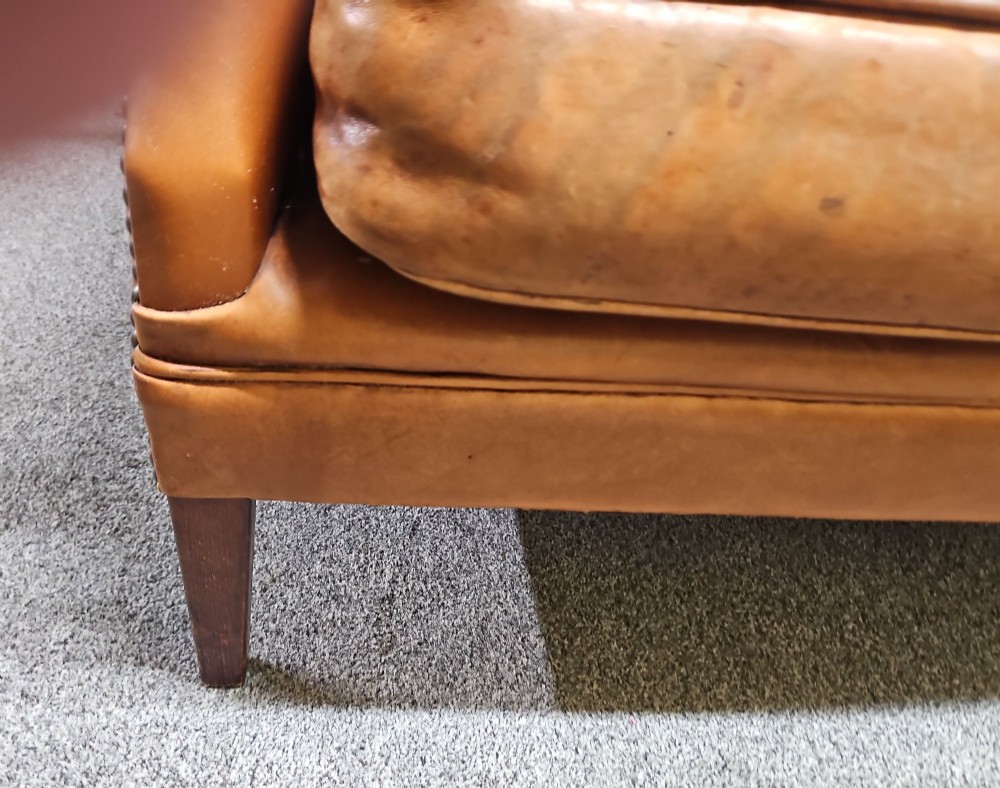 An Edwardian warm brown leather sofa featuring aged surface patina, loose seat cushions, and short tapered wooden legs. View II