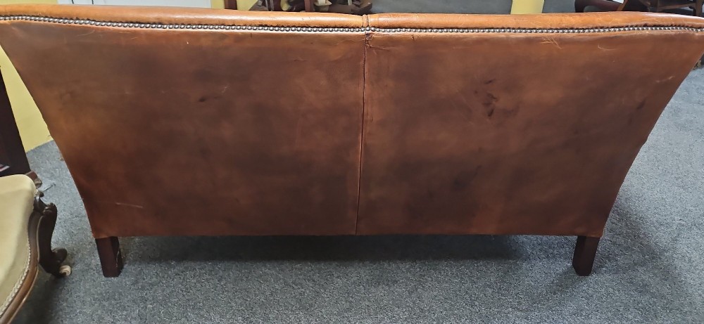 An Edwardian warm brown leather sofa featuring aged surface patina, loose seat cushions, and short tapered wooden legs. View VI