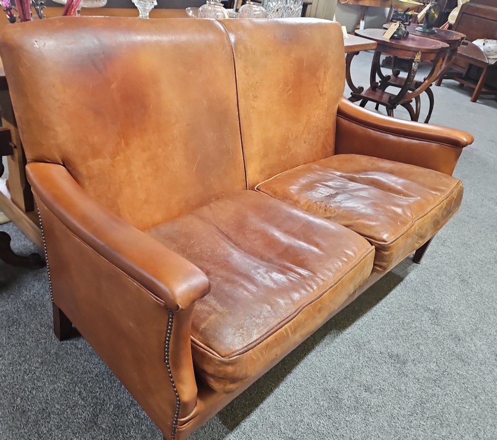 An Edwardian warm brown leather sofa featuring aged surface patina, loose seat cushions, and short tapered wooden legs. View VIII