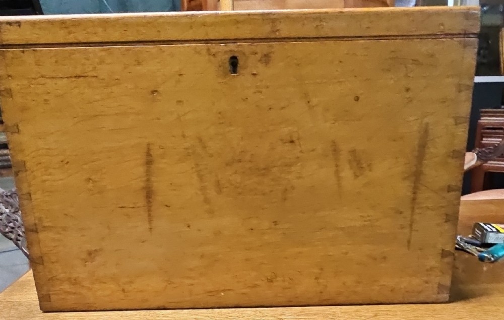 A rectangular light wooden antique storage box featuring visible dovetail corner joints and a central brass keyhole.