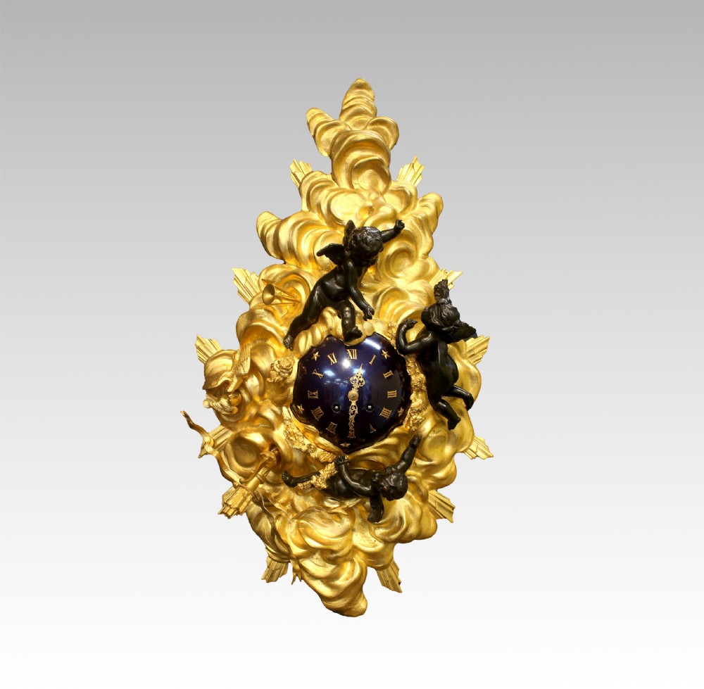 A 19th-century French cartel clock featuring a gilded bronze cloudburst frame, three dark patinated bronze cherub figures, and a deep blue enamel dial with Roman numerals. View VII