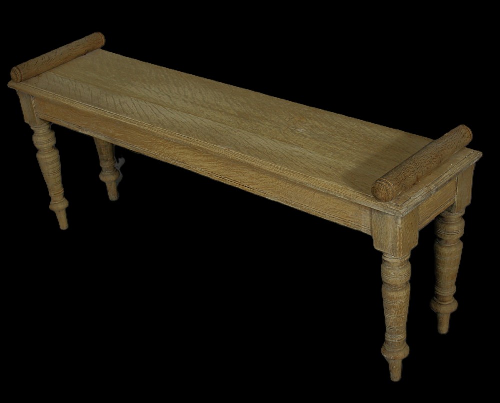 A long rectangular pale bleached oak window bench featuring turned wooden legs and cylindrical side bolsters.