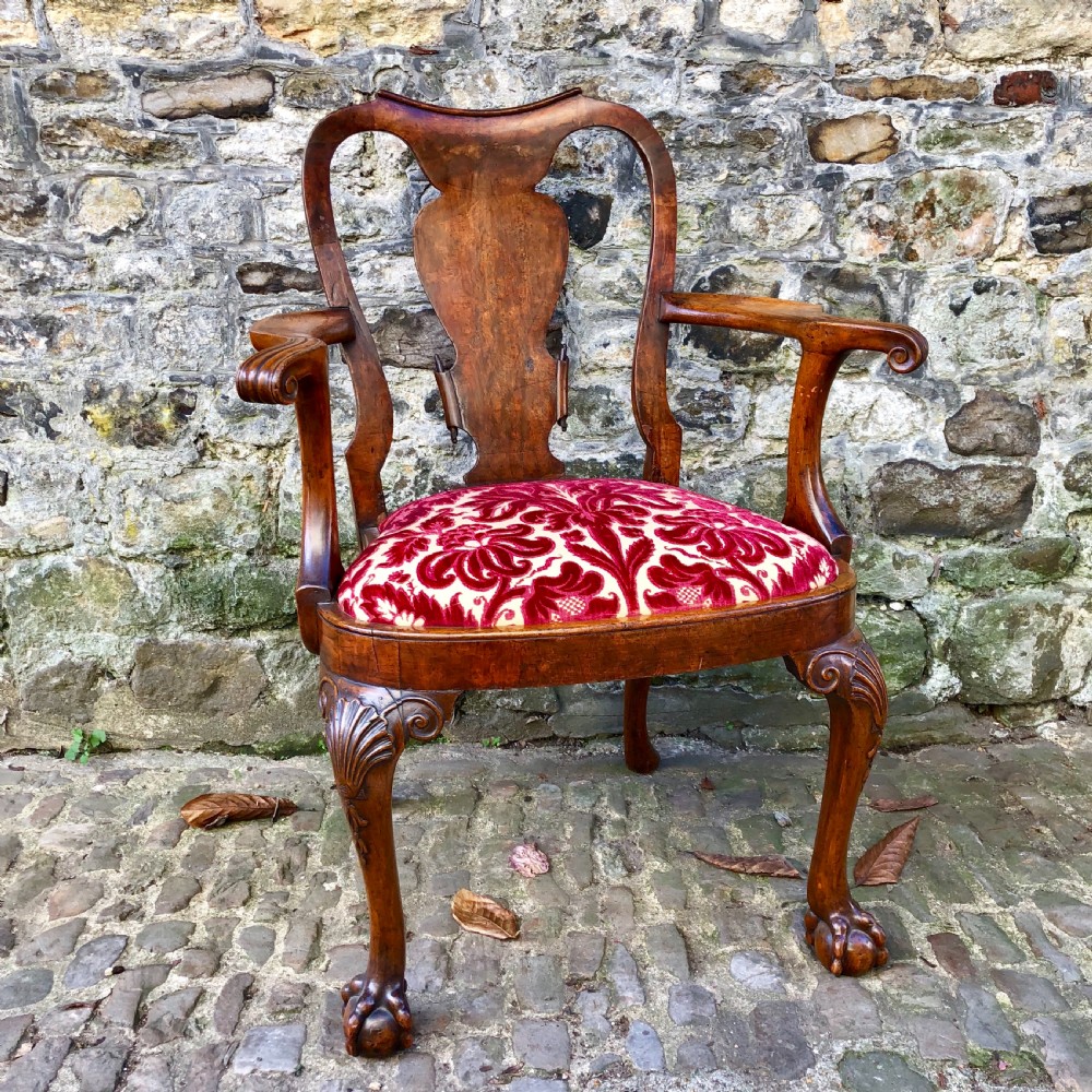 A George II style walnut armchair featuring a shaped splat back, carved cabriole legs with ball-and-claw feet, and a red patterned velvet seat.