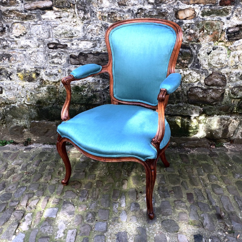 A Louis XV style open armchair crafted with a carved wooden frame, cabriole legs, and vibrant blue silk upholstery on the seat, backrest, and padded armrests.