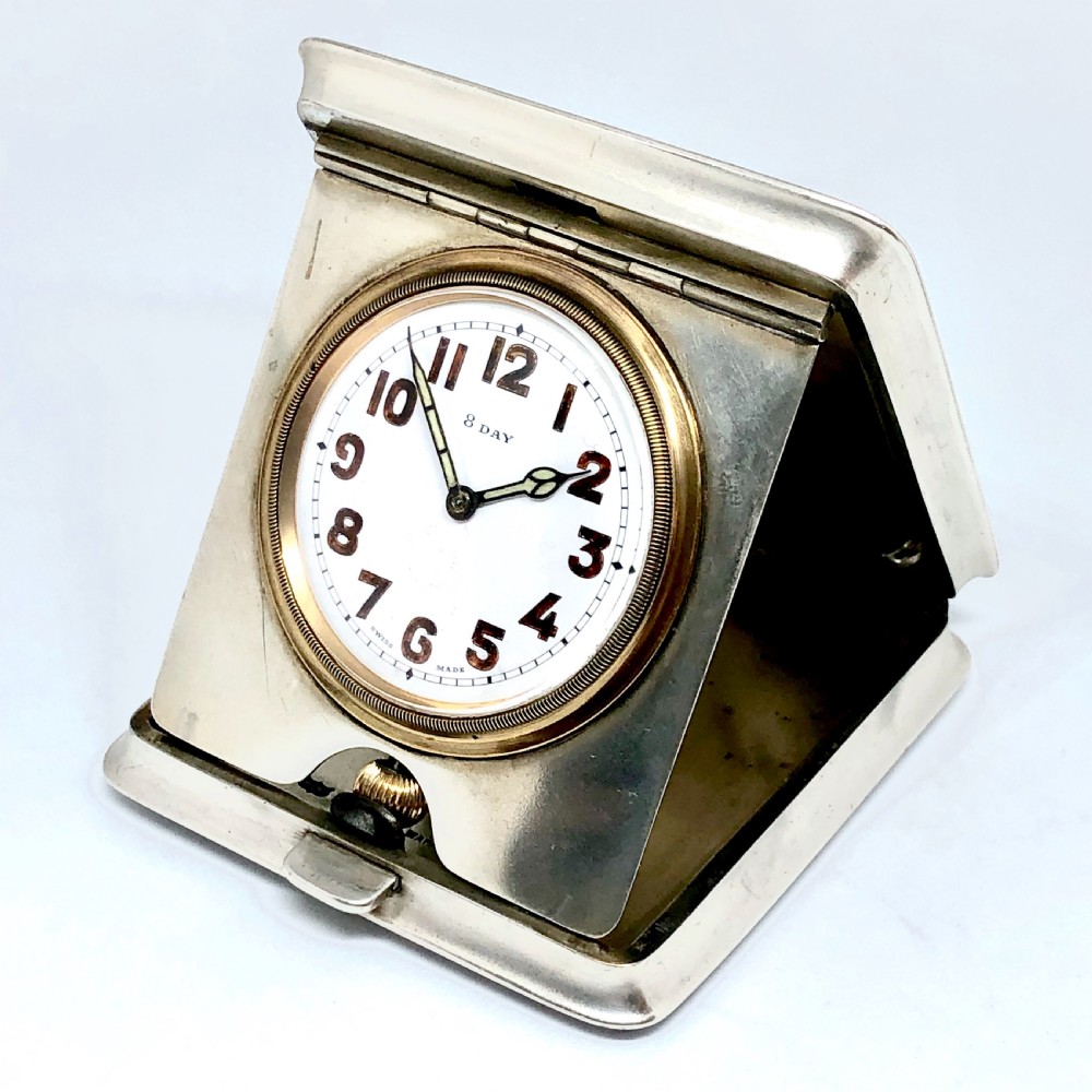 An early 20th-century silver folding travel clock by Mappin and Webb, featuring a square metallic case with a circular white dial and dark Arabic numerals. View VI