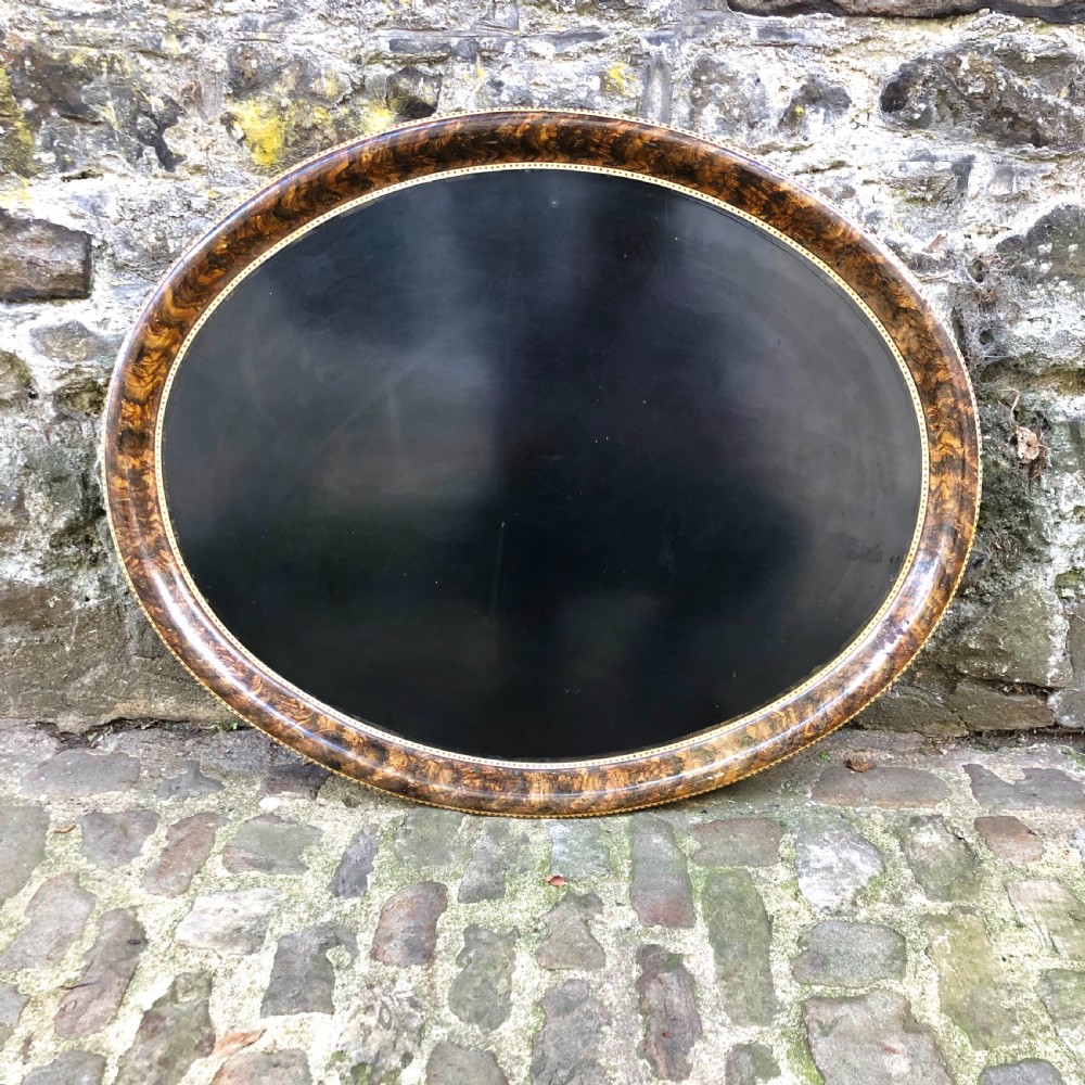 A mid-nineteenth century oval tole peinte tray featuring a black lacquered centre framed by a faux tortoiseshell rim with gilt detail.