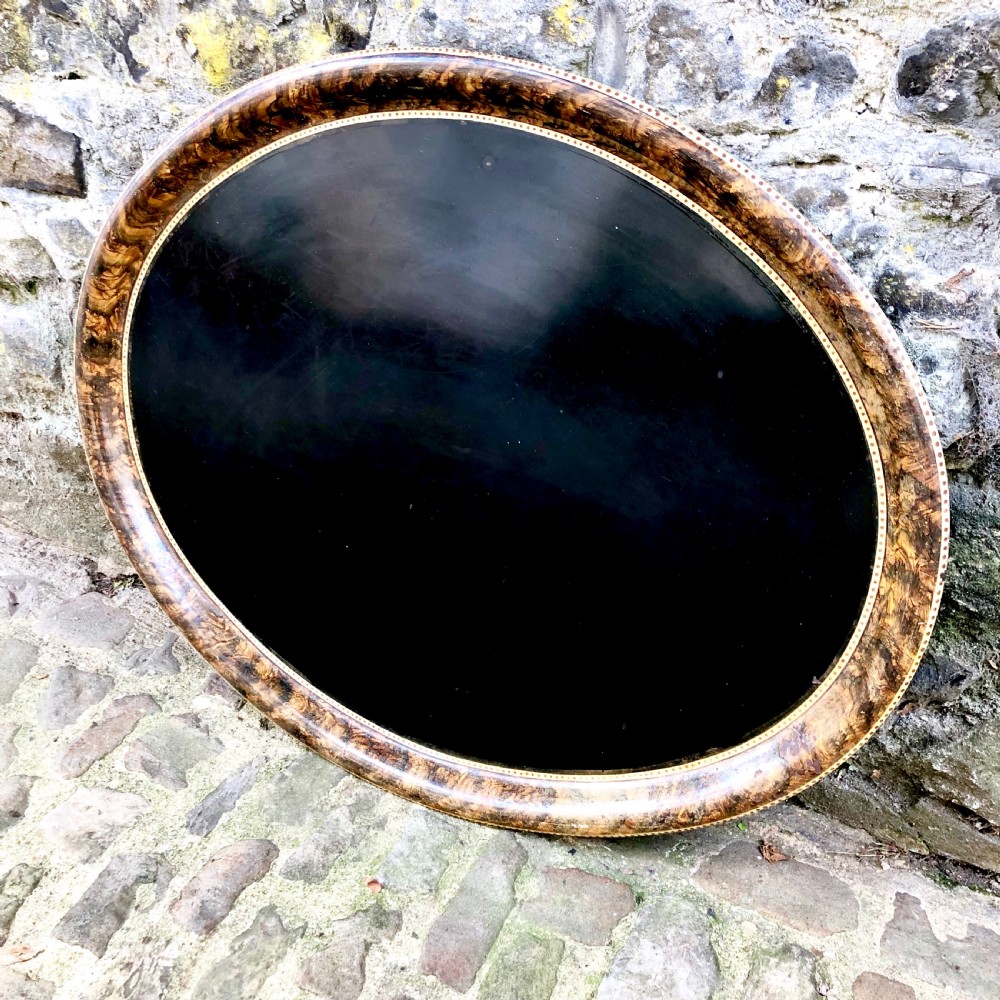A mid-nineteenth century oval tole peinte tray featuring a black lacquered centre framed by a faux tortoiseshell rim with gilt detail. View II