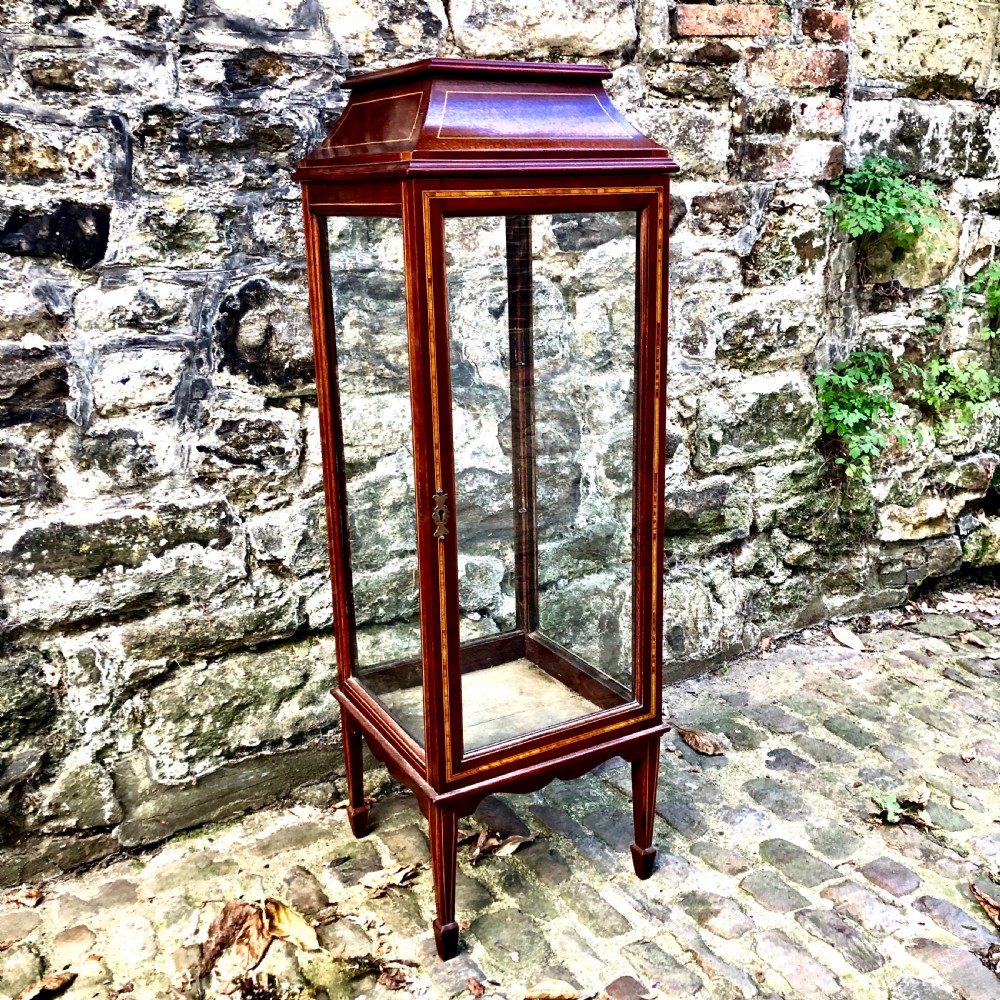 A tall, narrow Edwardian mahogany display cabinet with glazed side panels, fine wood stringing inlay, a single glass front door with a brass keyhole, and square tapered legs. View IV