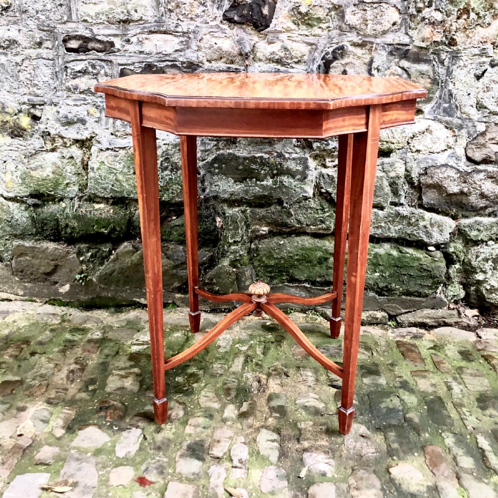 An Edwardian satinwood occasional table with a shaped top, crossbanded edging, square tapered legs, and an X-frame stretcher with a central finial.