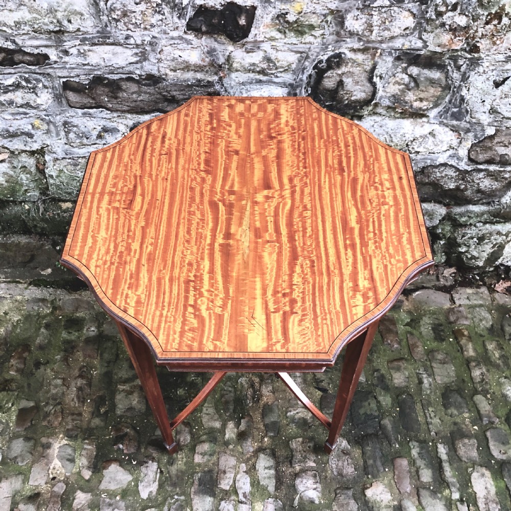 An Edwardian satinwood occasional table with a shaped top, crossbanded edging, square tapered legs, and an X-frame stretcher with a central finial. View III