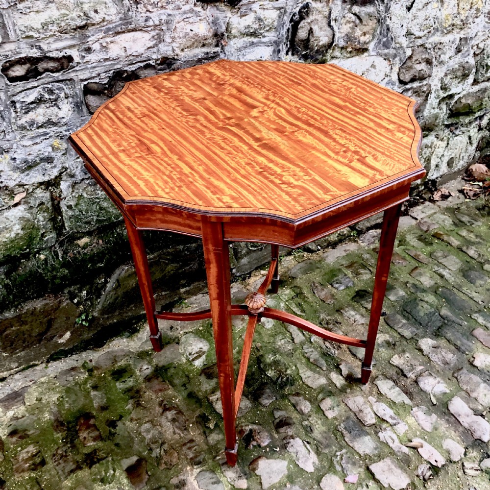 An Edwardian satinwood occasional table with a shaped top, crossbanded edging, square tapered legs, and an X-frame stretcher with a central finial. View IV