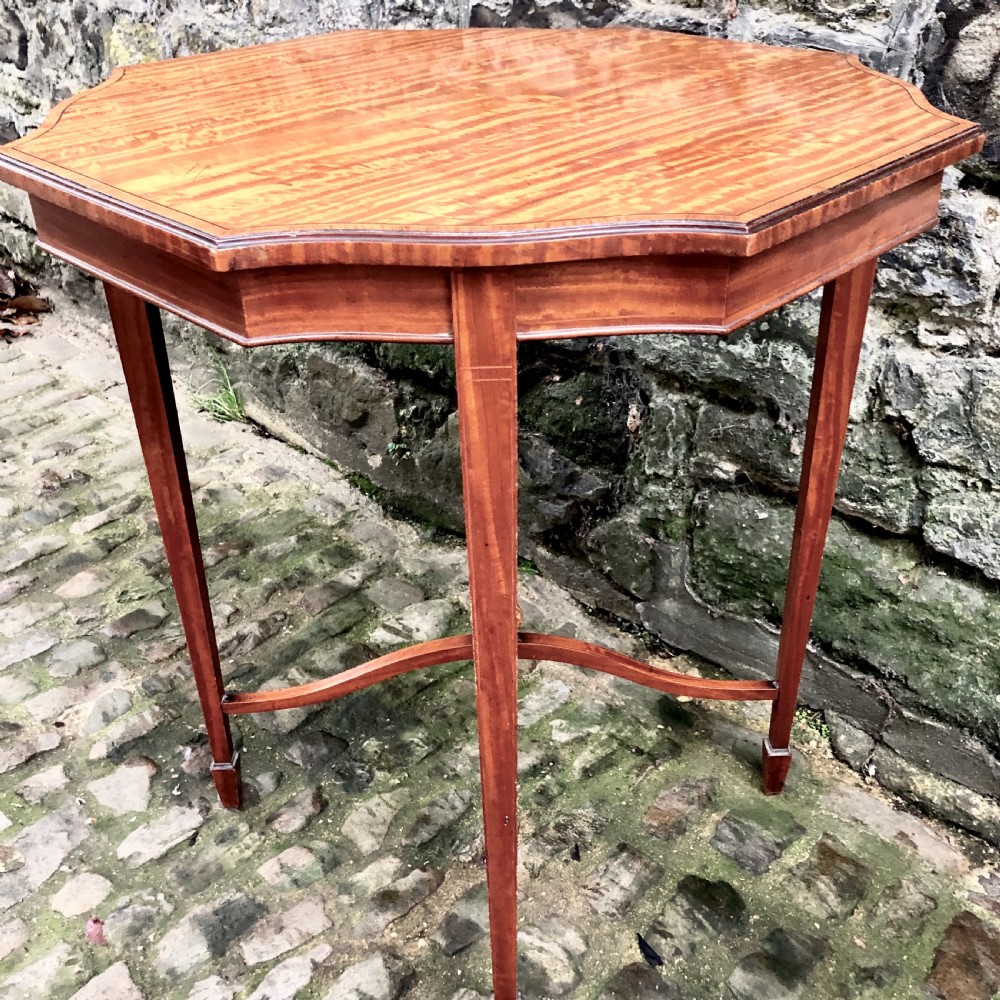 An Edwardian satinwood occasional table with a shaped top, crossbanded edging, square tapered legs, and an X-frame stretcher with a central finial. View VI