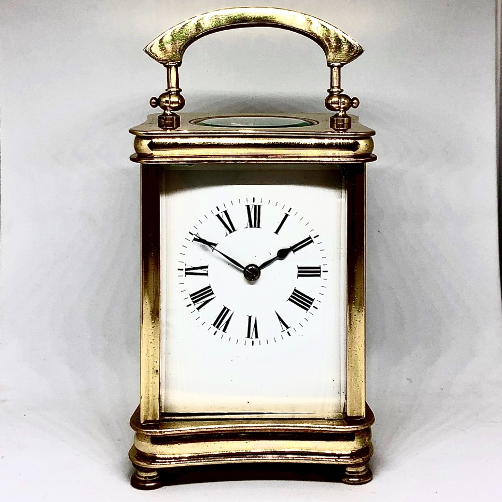 A late 19th-century French gilt brass carriage clock featuring a rectangular case with bevelled glass panels, an arched top handle, and a white enamel dial with black Roman numerals.