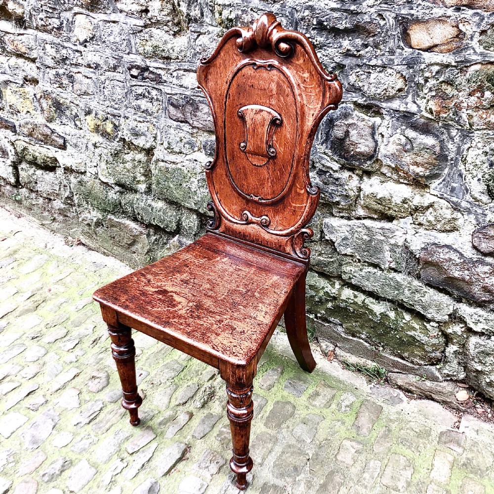 An early Victorian oak hall chair featuring a carved shield-shaped backrest, solid wooden seat, and turned front legs. View II