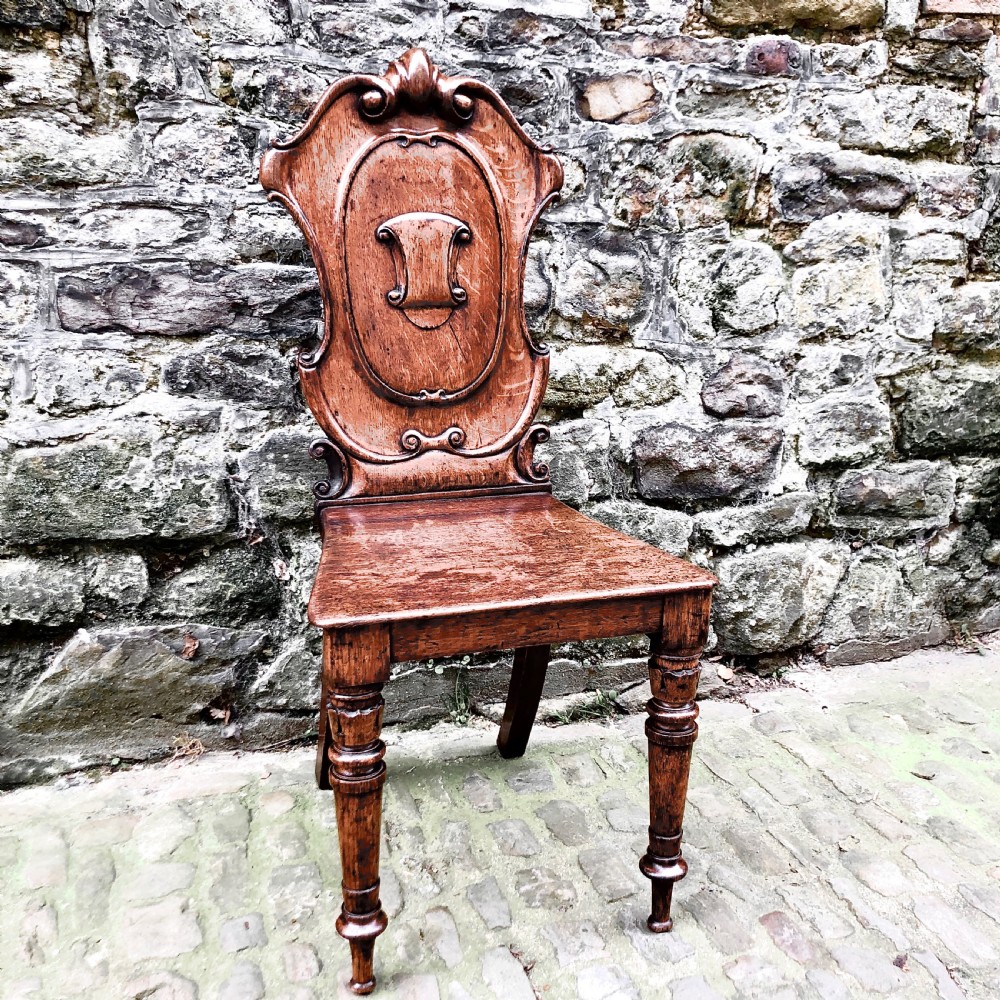 An early Victorian oak hall chair featuring a carved shield-shaped backrest, solid wooden seat, and turned front legs. View III