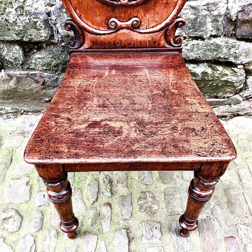 An early Victorian oak hall chair featuring a carved shield-shaped backrest, solid wooden seat, and turned front legs. View IV