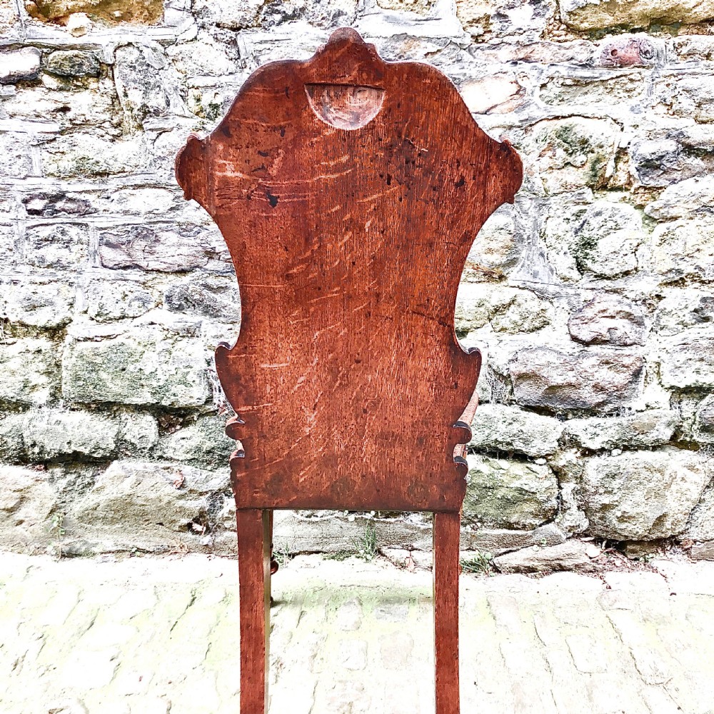 An early Victorian oak hall chair featuring a carved shield-shaped backrest, solid wooden seat, and turned front legs. View VII