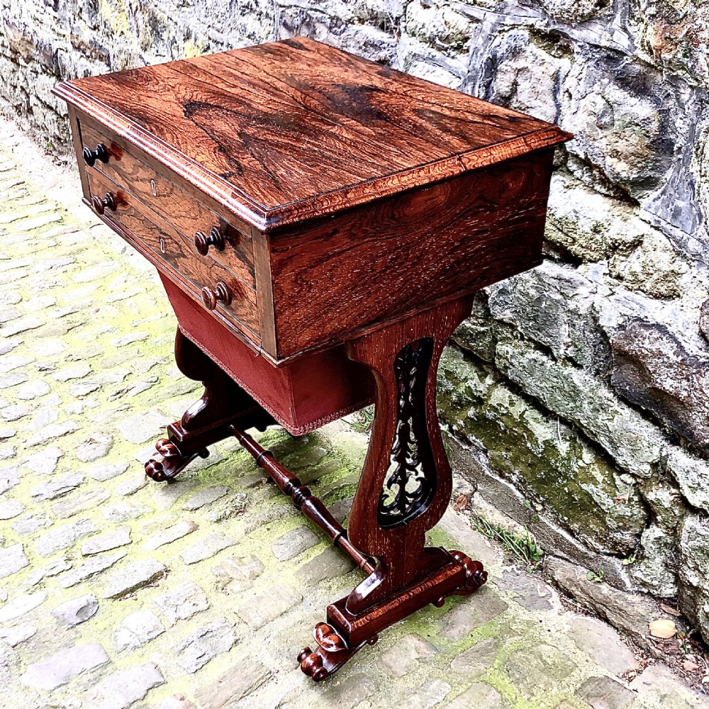 A William IV rosewood work table featuring two drawer fronts, turned knobs, keyhole escutcheons, a red fabric drop pouch, and carved end supports. View II