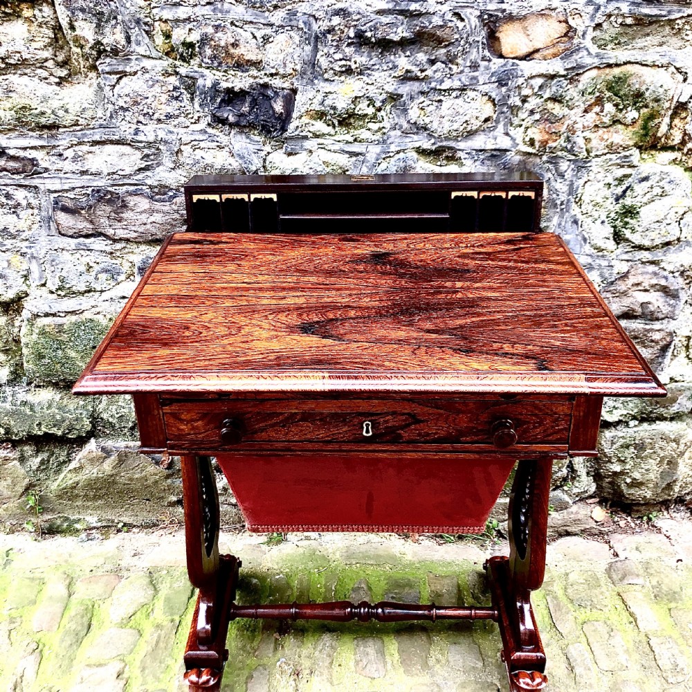 A William IV rosewood work table featuring two drawer fronts, turned knobs, keyhole escutcheons, a red fabric drop pouch, and carved end supports. View IV