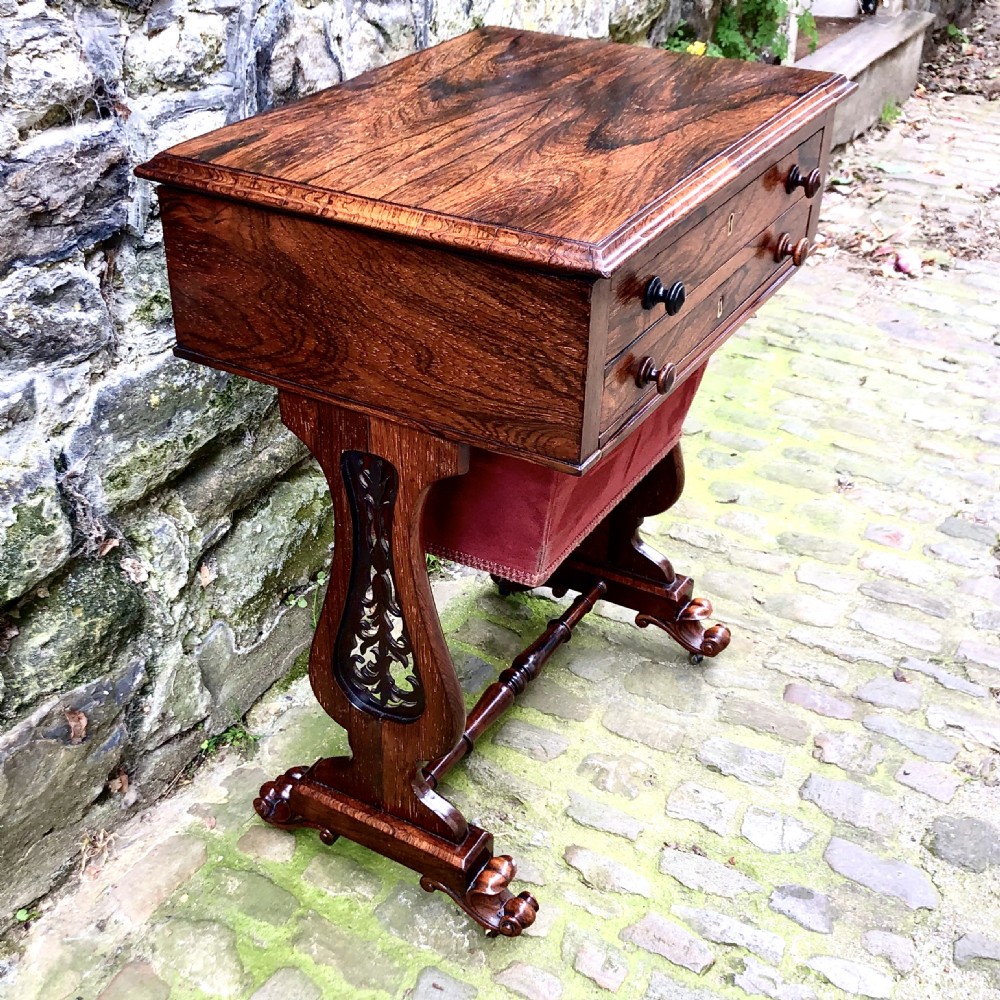 A William IV rosewood work table featuring two drawer fronts, turned knobs, keyhole escutcheons, a red fabric drop pouch, and carved end supports. View V
