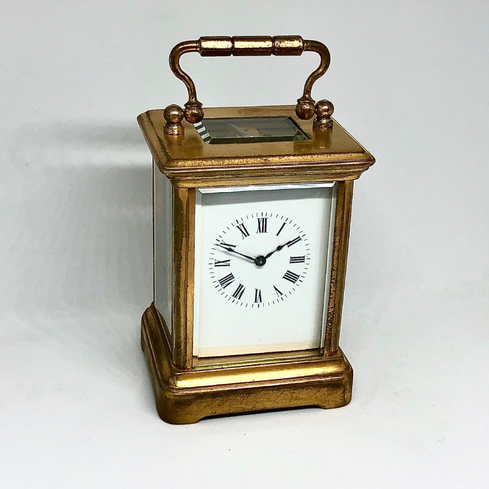 A late nineteenth-century miniature French gilt brass carriage clock featuring a rectangular case with glass panels, a curved top handle, and a white enamel dial with Roman numerals.