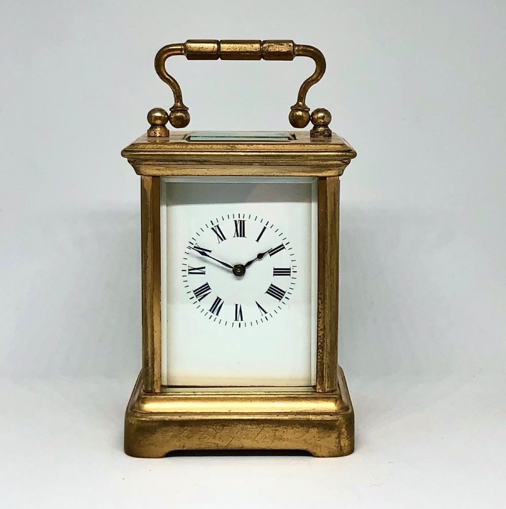 A late nineteenth-century miniature French gilt brass carriage clock featuring a rectangular case with glass panels, a curved top handle, and a white enamel dial with Roman numerals. View II