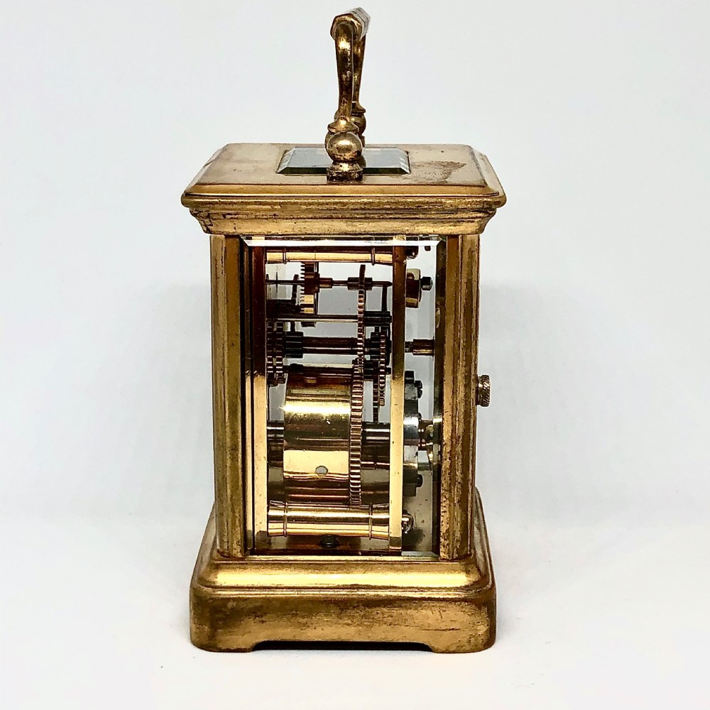 A late nineteenth-century miniature French gilt brass carriage clock featuring a rectangular case with glass panels, a curved top handle, and a white enamel dial with Roman numerals. View IV