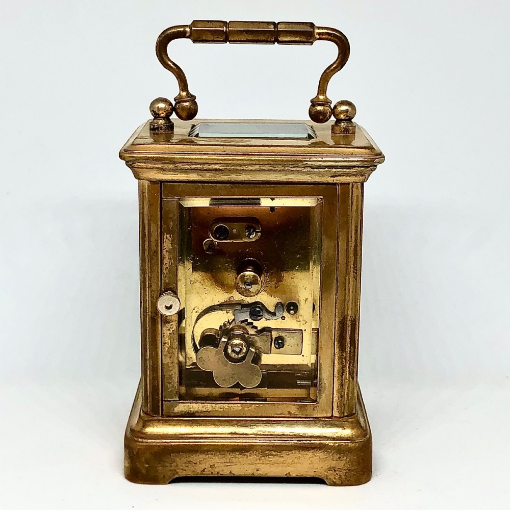 A late nineteenth-century miniature French gilt brass carriage clock featuring a rectangular case with glass panels, a curved top handle, and a white enamel dial with Roman numerals. View V