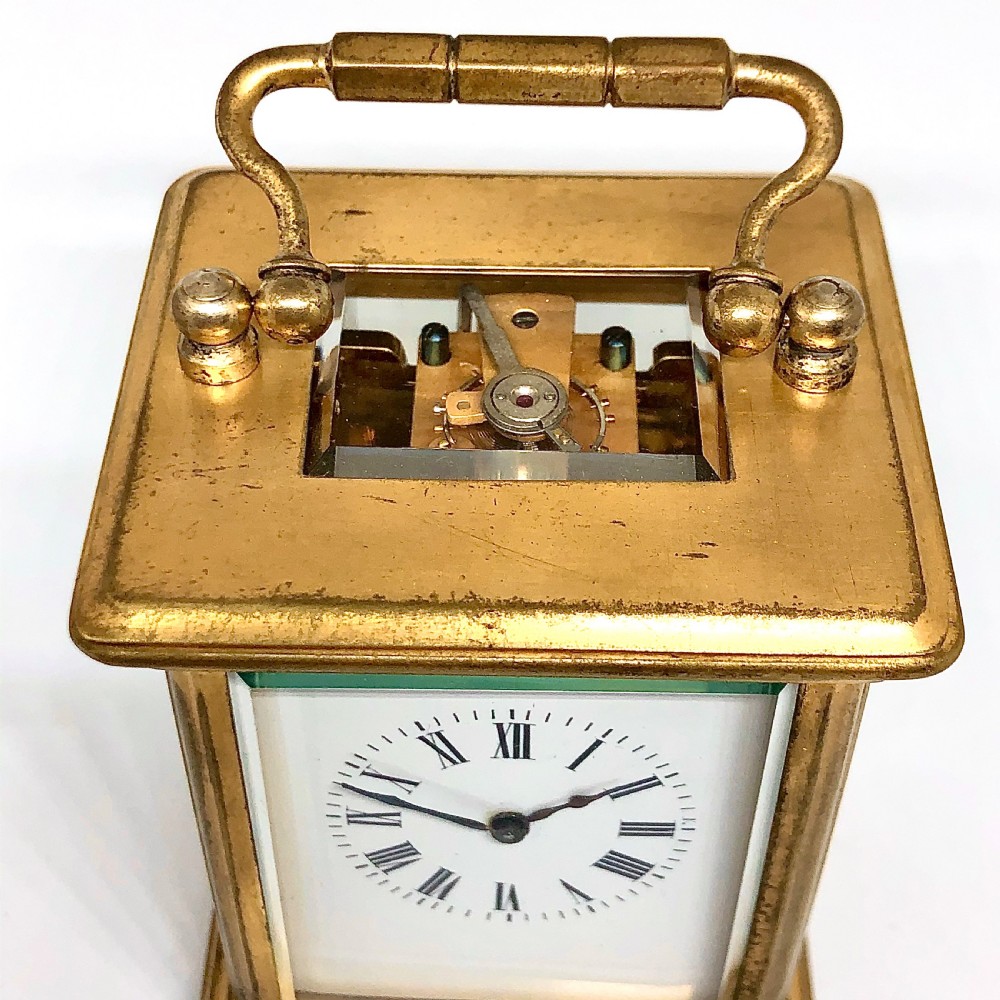 A late nineteenth-century miniature French gilt brass carriage clock featuring a rectangular case with glass panels, a curved top handle, and a white enamel dial with Roman numerals. View VI