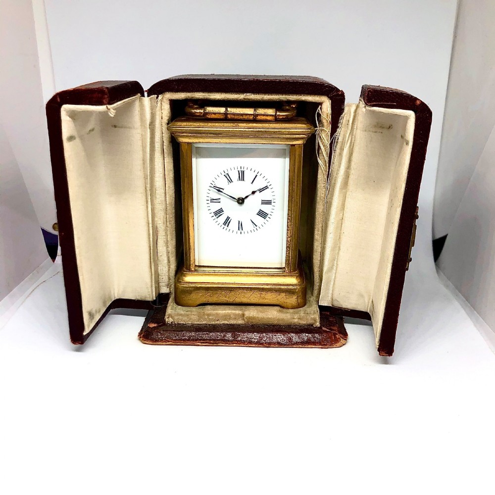 A late nineteenth-century miniature French gilt brass carriage clock featuring a rectangular case with glass panels, a curved top handle, and a white enamel dial with Roman numerals. View VII