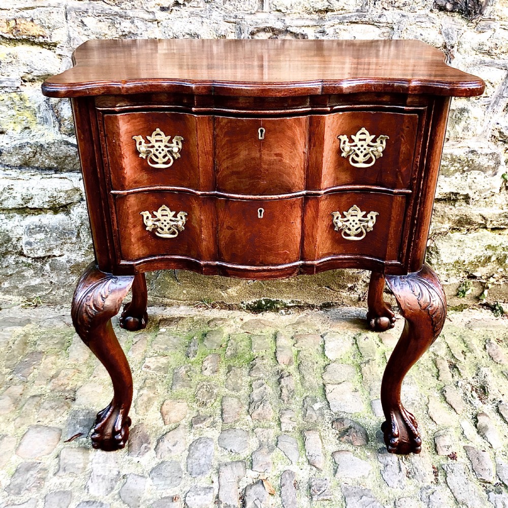 A Portuguese mahogany two-drawer commode featuring serpentine drawer fronts, decorative brass escutcheons and handles, and carved cabriole legs ending in claw feet.