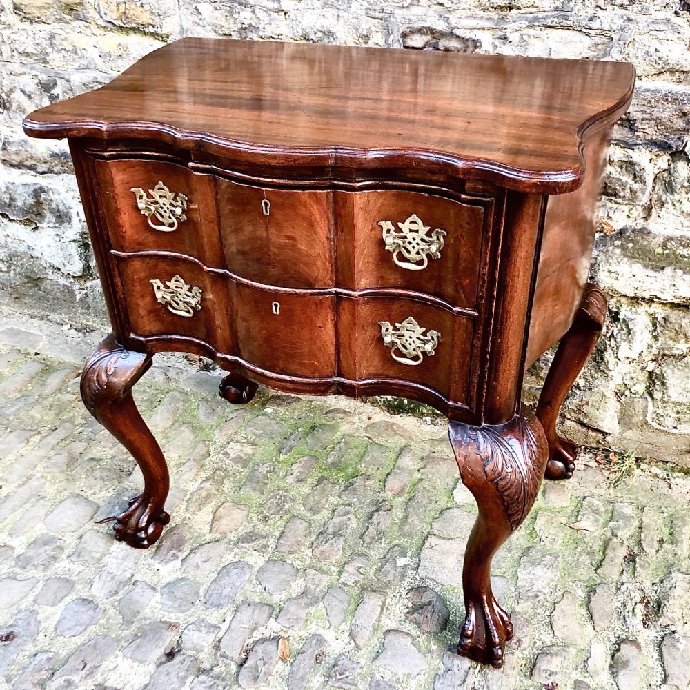 A Portuguese mahogany two-drawer commode featuring serpentine drawer fronts, decorative brass escutcheons and handles, and carved cabriole legs ending in claw feet. View II