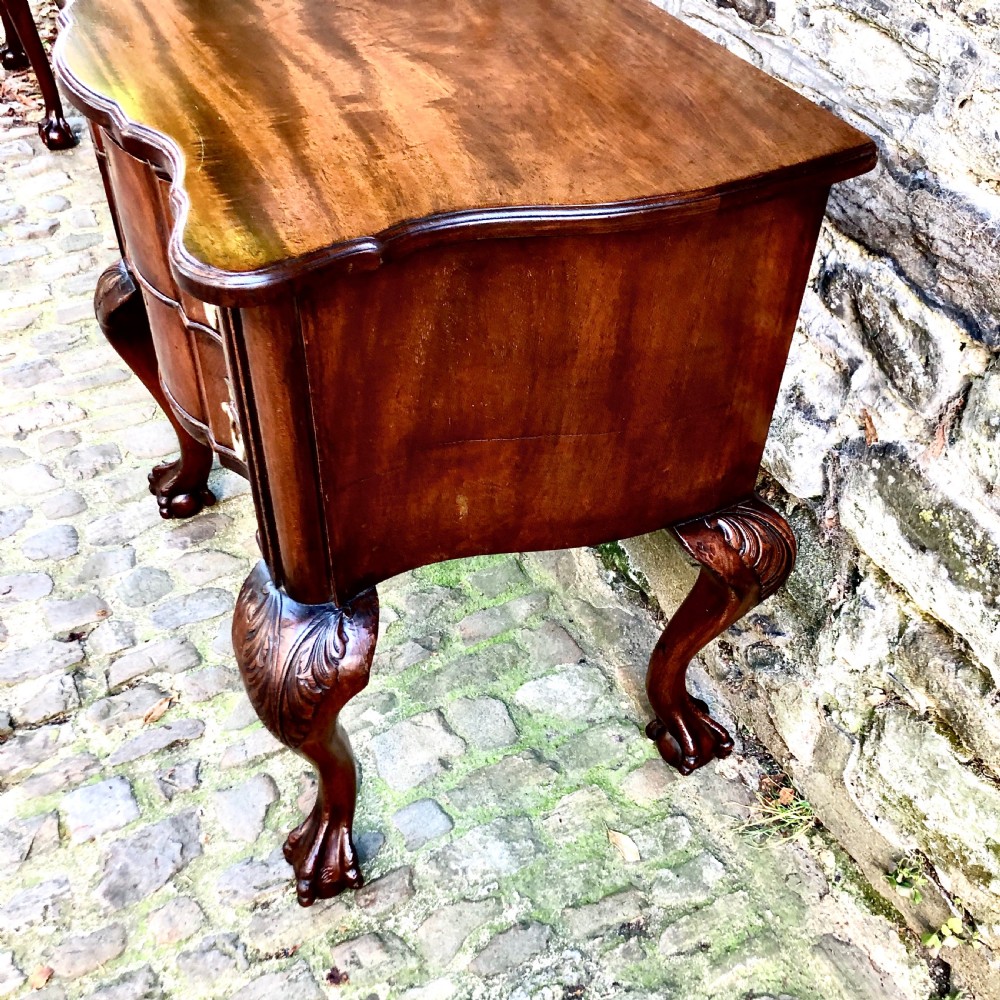 A Portuguese mahogany two-drawer commode featuring serpentine drawer fronts, decorative brass escutcheons and handles, and carved cabriole legs ending in claw feet. View IV