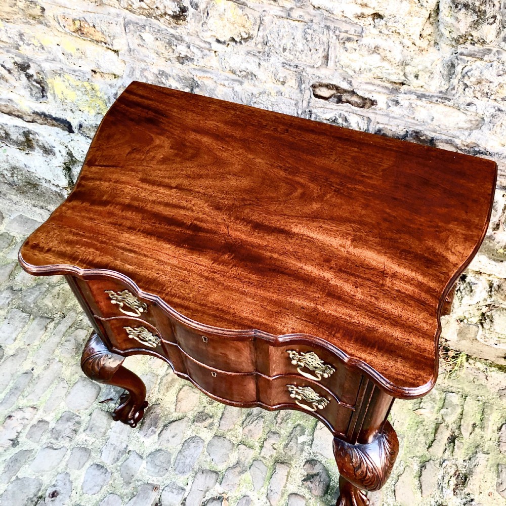 A Portuguese mahogany two-drawer commode featuring serpentine drawer fronts, decorative brass escutcheons and handles, and carved cabriole legs ending in claw feet. View V