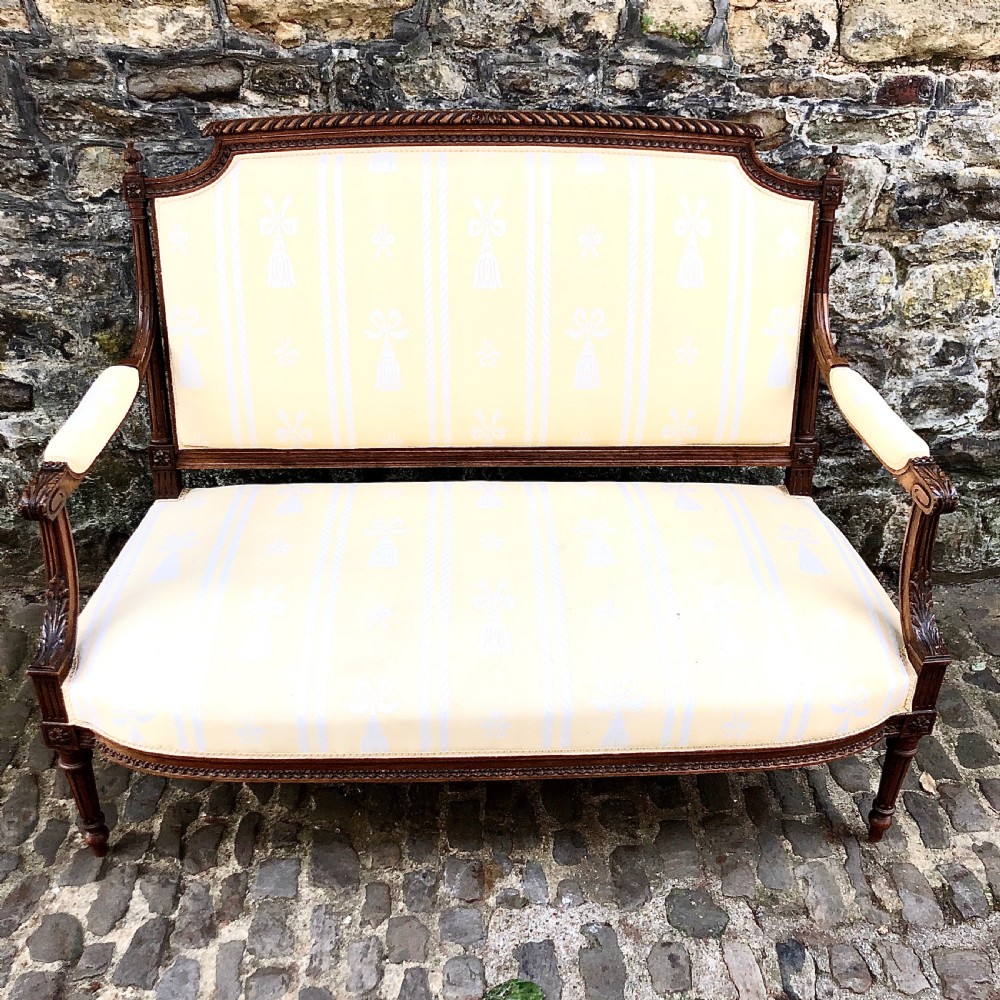 A French Second Empire carved walnut sofa featuring a cream and pale yellow striped upholstered back and seat with padded armrests and fluted legs.