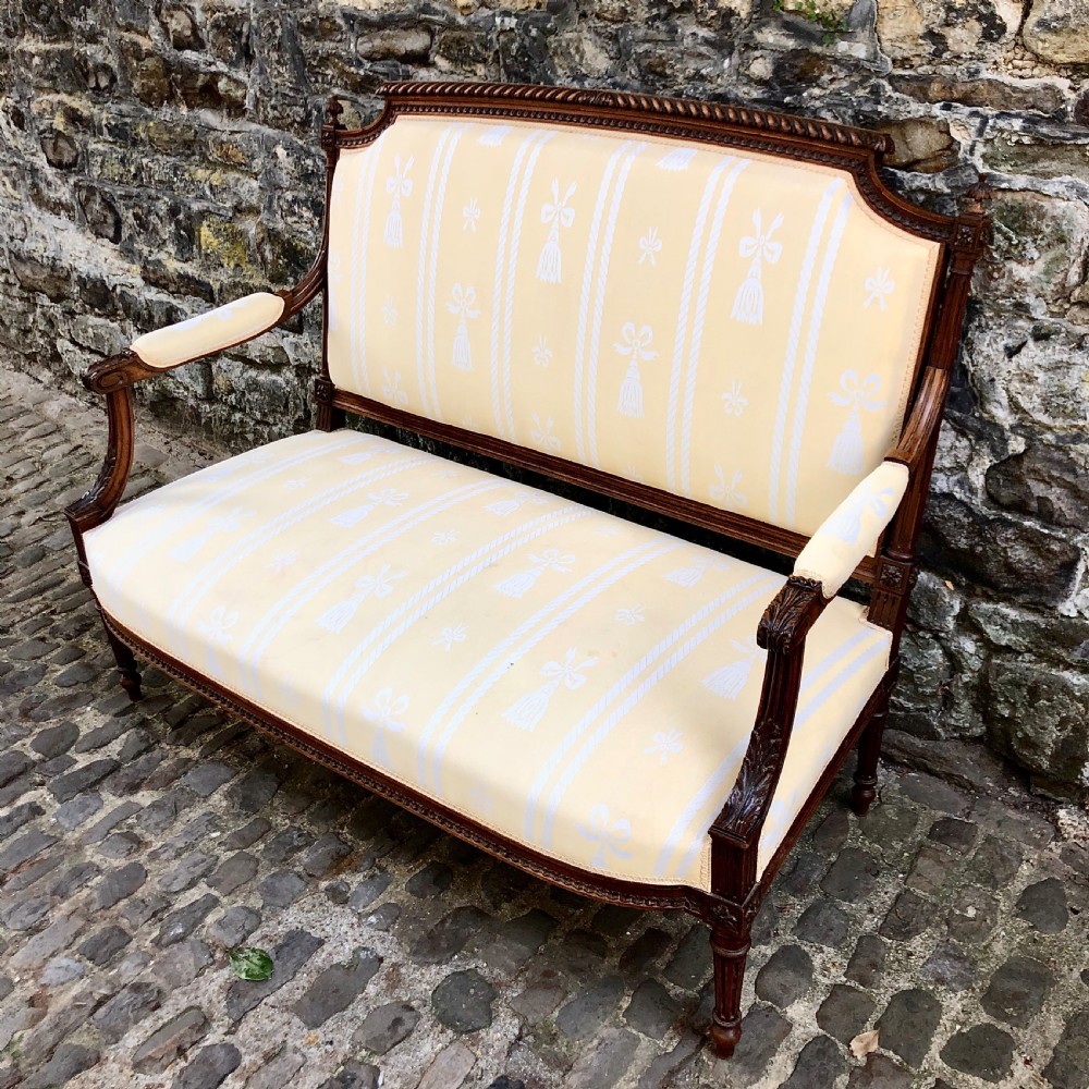 A French Second Empire carved walnut sofa featuring a cream and pale yellow striped upholstered back and seat with padded armrests and fluted legs. View IV