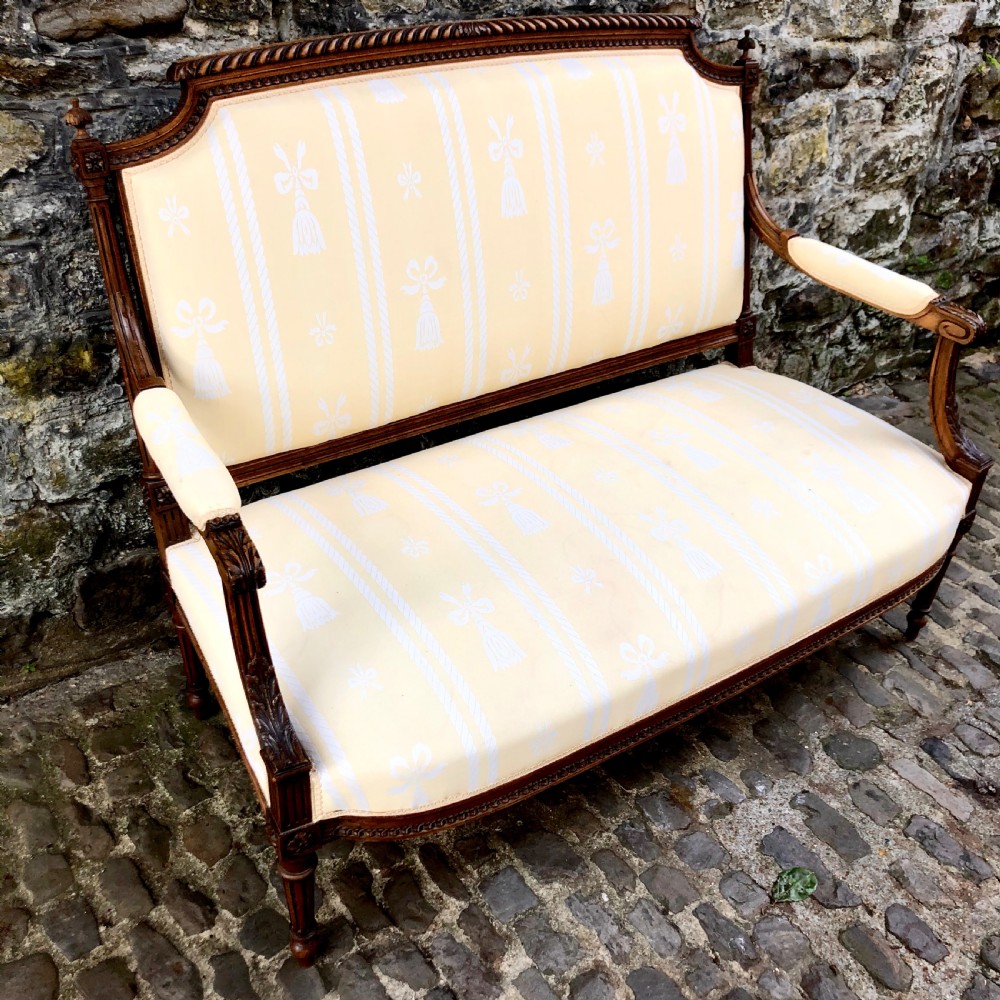 A French Second Empire carved walnut sofa featuring a cream and pale yellow striped upholstered back and seat with padded armrests and fluted legs. View V