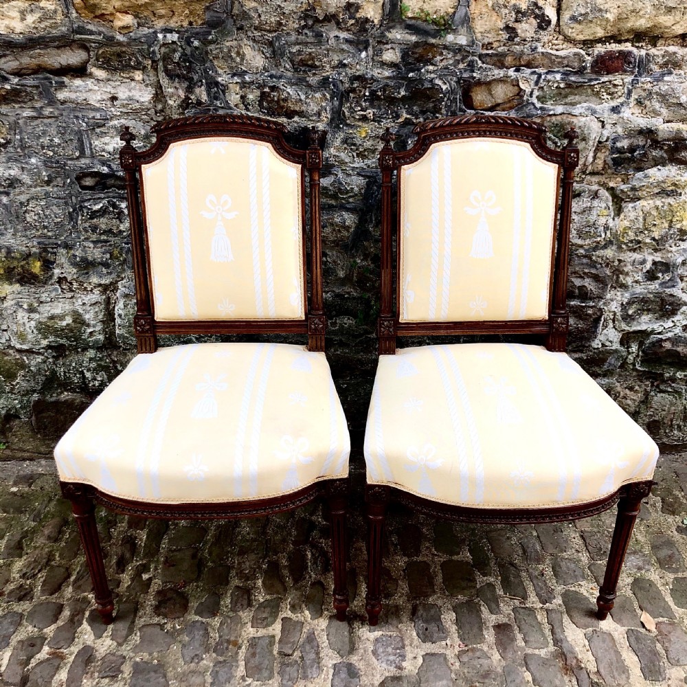 A pair of antique French Second Empire carved walnut side chairs upholstered in a cream patterned damask fabric featuring fluted legs.
