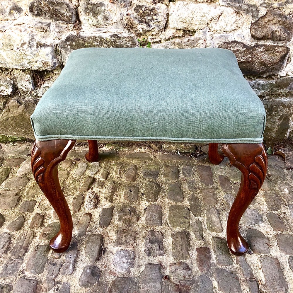 A 19th-century upholstered footstool featuring sage green fabric on a carved walnut frame with cabriole legs.