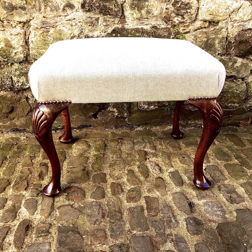 A 19th-century walnut dressing table stool featuring carved cabriole legs with shell knee detailing, brass studded trim, and a cream upholstered linen cushion.