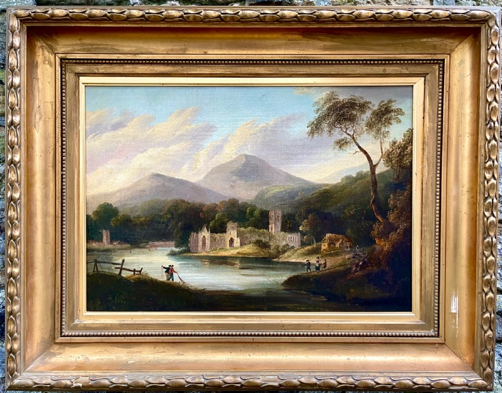 An early nineteenth-century oil painting depicting Tintern Abbey beside a river, surrounded by mountains and set within a carved gold frame.