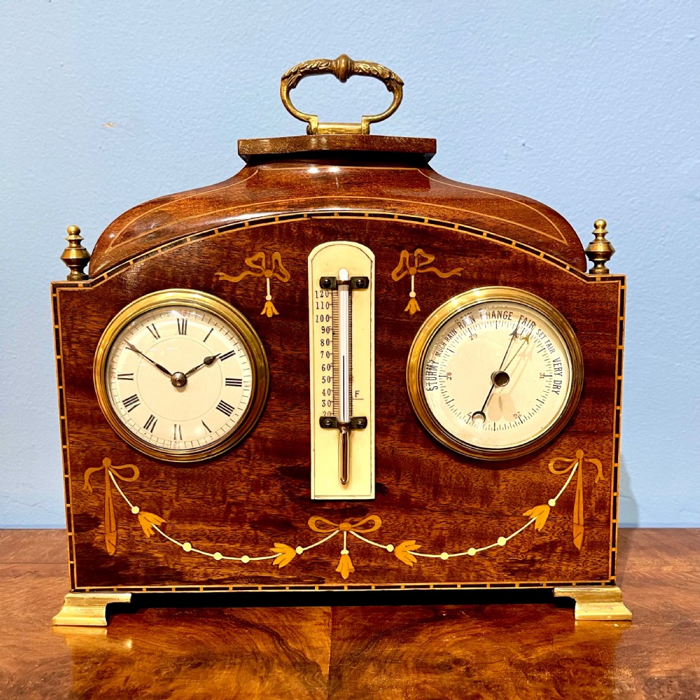 An Edwardian inlaid mahogany mantel clock featuring a clock face on the left, an aneroid barometer on the right, and a vertical thermometer in the centre, finished with a brass carrying handle and marquetry ribbon swags.