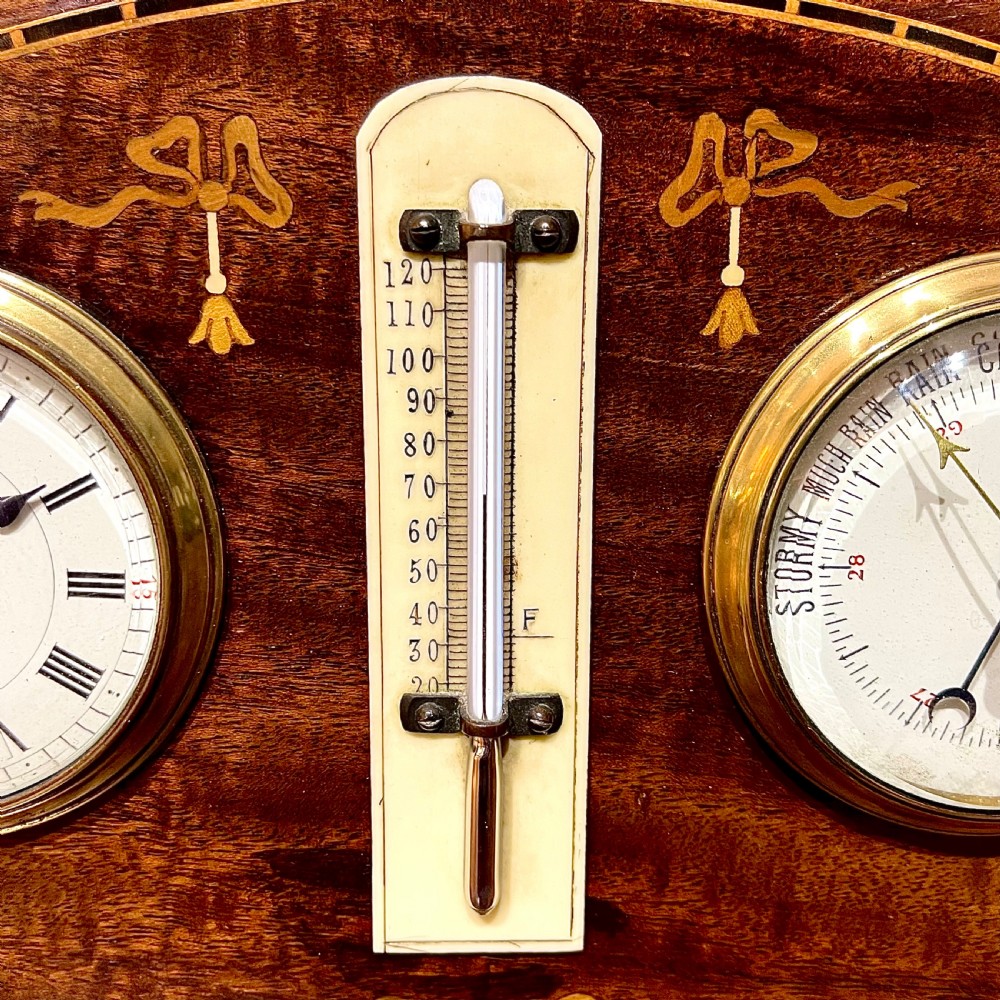 An Edwardian inlaid mahogany mantel clock featuring a clock face on the left, an aneroid barometer on the right, and a vertical thermometer in the centre, finished with a brass carrying handle and marquetry ribbon swags. View II