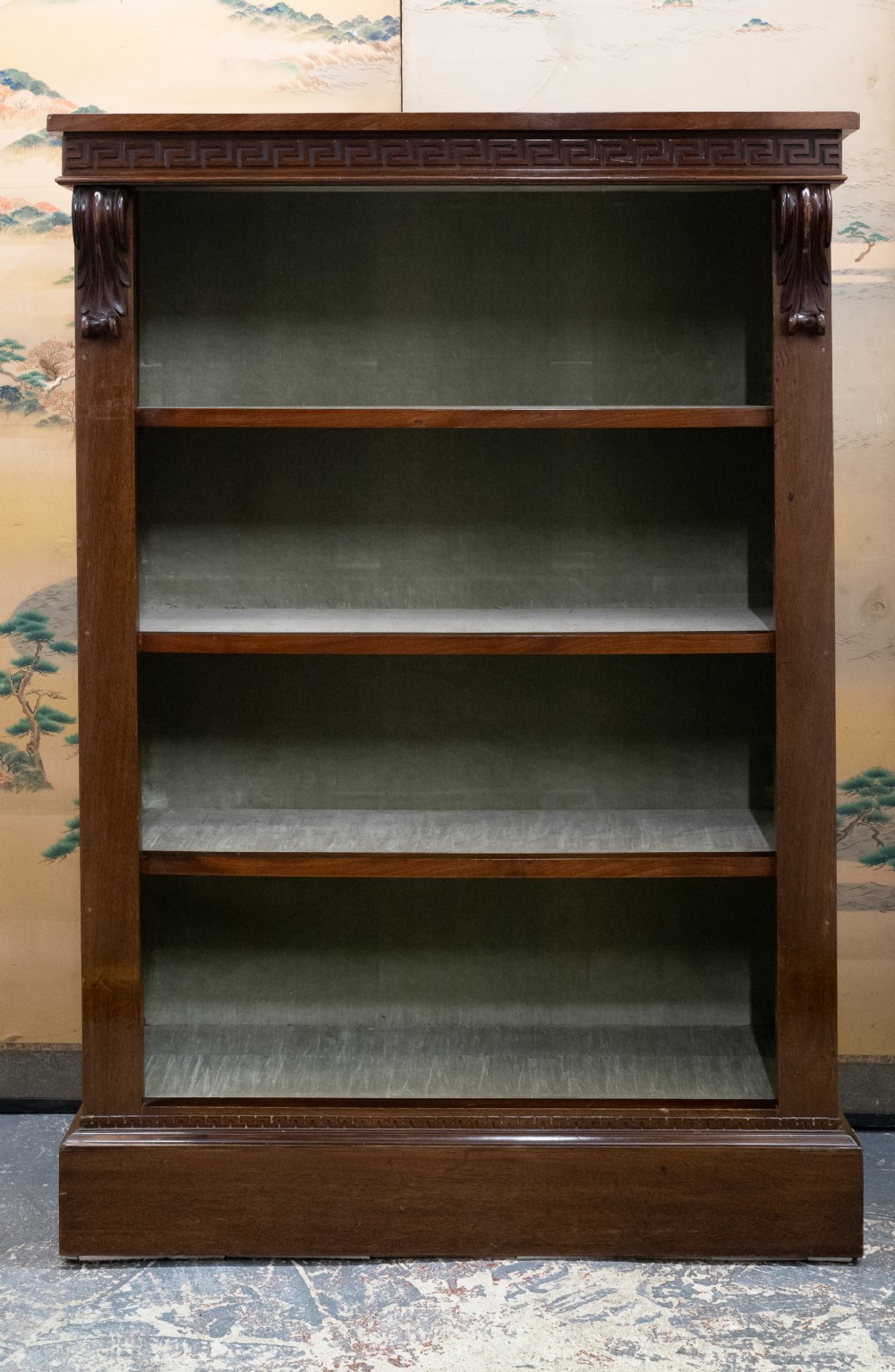 A dark mahogany open bookcase featuring four shelves, a carved Greek key pattern along the top frieze, and carved side corbels.