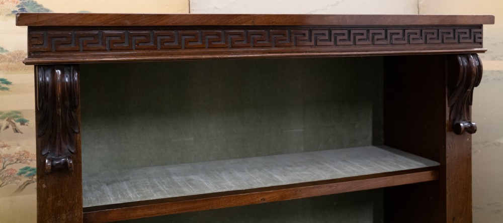 A dark mahogany open bookcase featuring four shelves, a carved Greek key pattern along the top frieze, and carved side corbels. View III